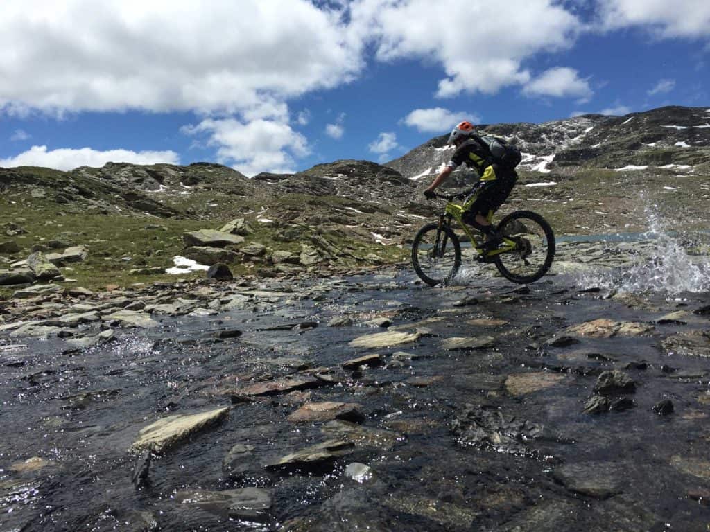 Un ragazzo in mountain bike attraversa un torrente sulla montagna.