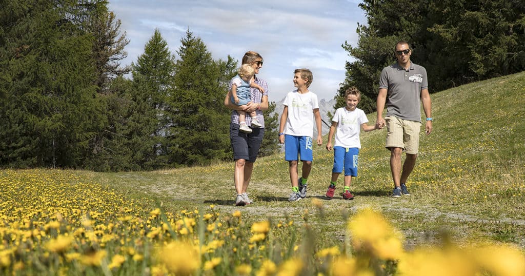 Una famiglia con bambini che attraversa un campo di fiori durante una passeggiata a Bormio.