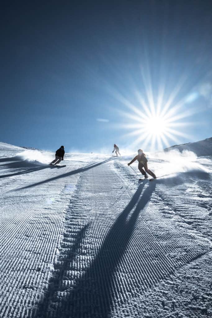 Tre persone superano la paura di sciare scendendo un pendio innevato con il sole alle spalle