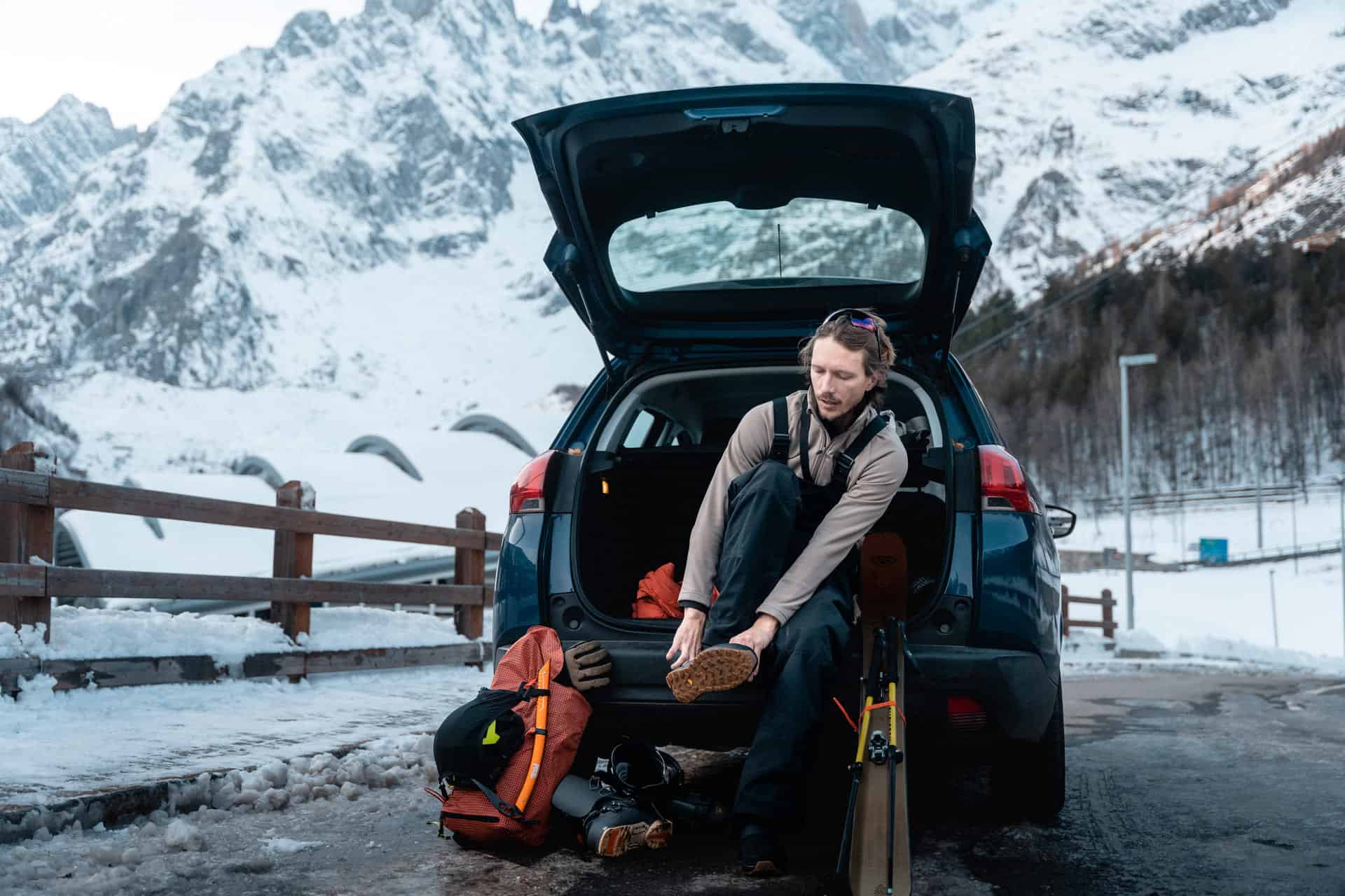 Uomo appoggiato al bagagliaio di un'auto si prepara per un'attività invernale all'aperto in montagna con una coperta isotermica.