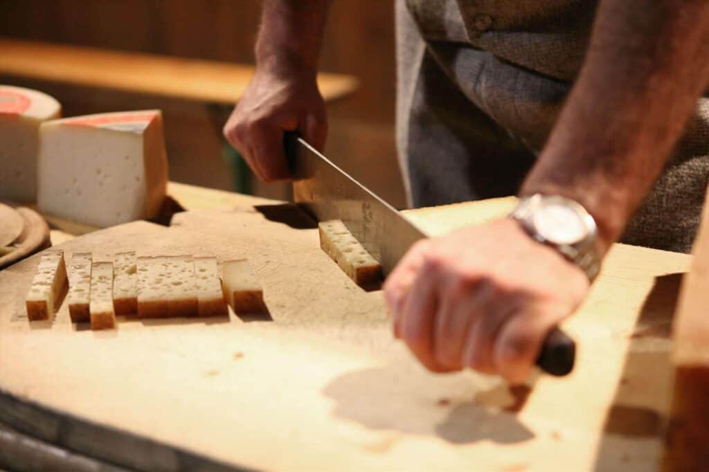 Una persona che affetta un formaggio tipico della cucina valtellinese su un tagliere di legno.